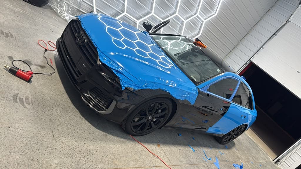 District 3 Performance installer applying a blue vehicle wrap to an Audi A6, half-wrapped mid-install